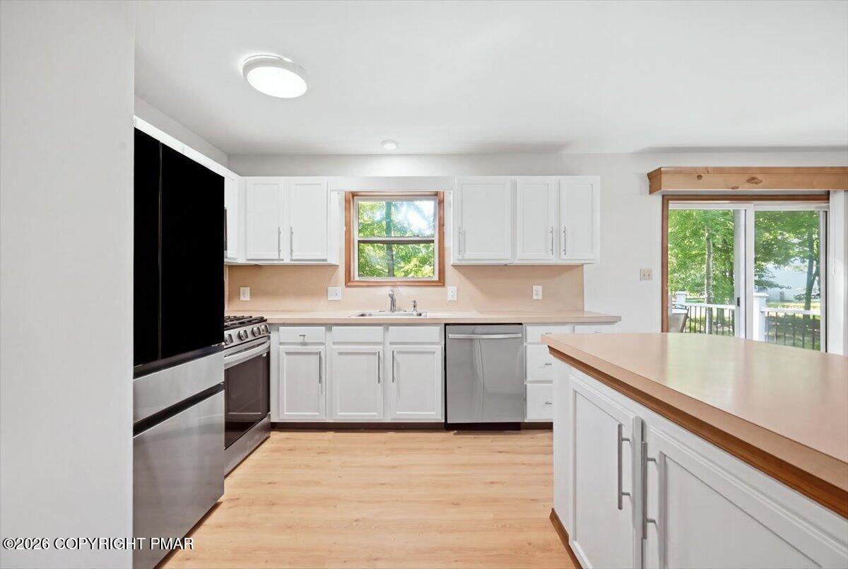 Kitchen with white cabinets, stainless steel appliances, and an island beside a sliding glass door to the deck.