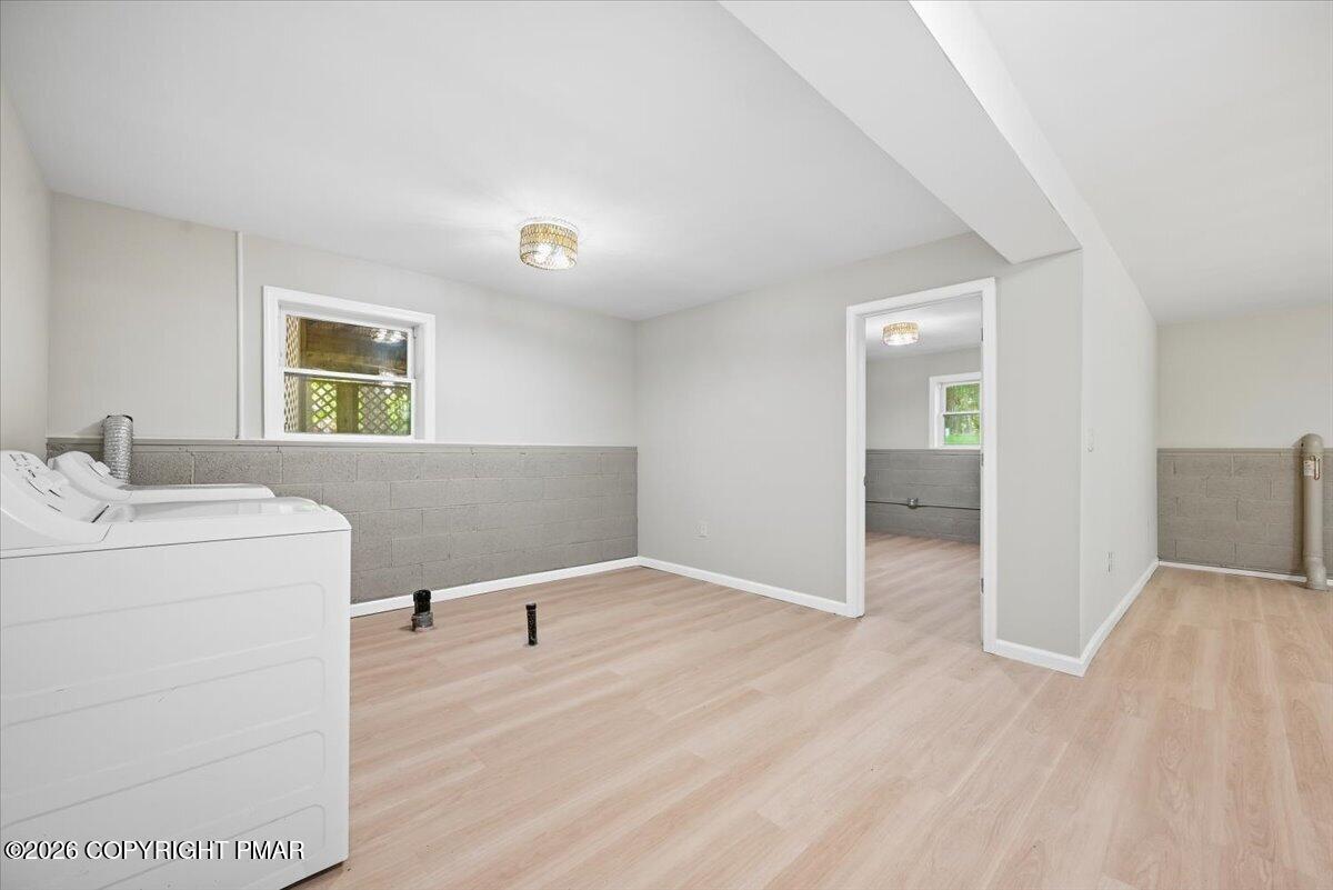 Laundry room with light wood-look floors, gray block wainscoting, and a washer and dryer.