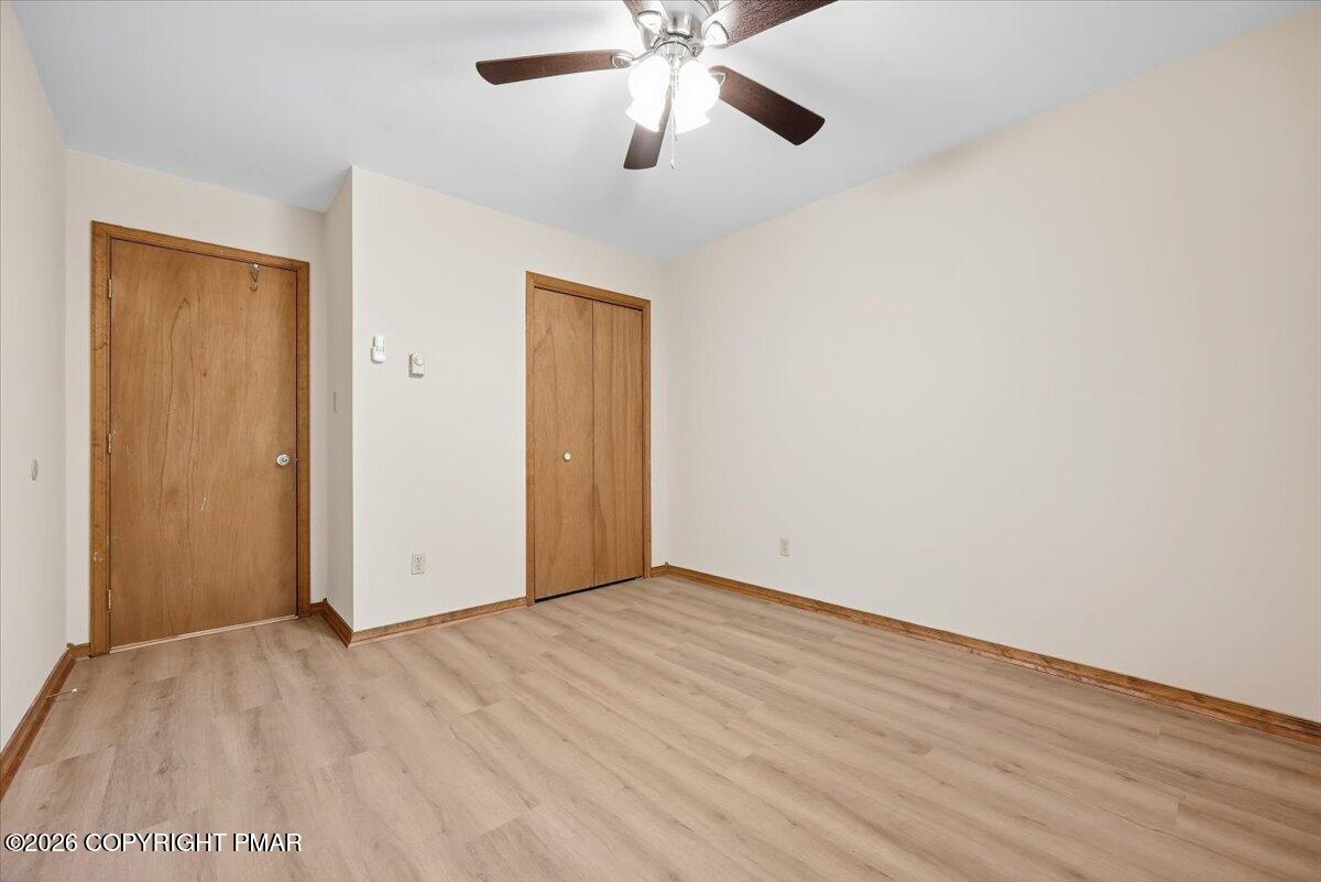 Vacant room with light wood-look flooring, two wooden doors, and a ceiling fan.