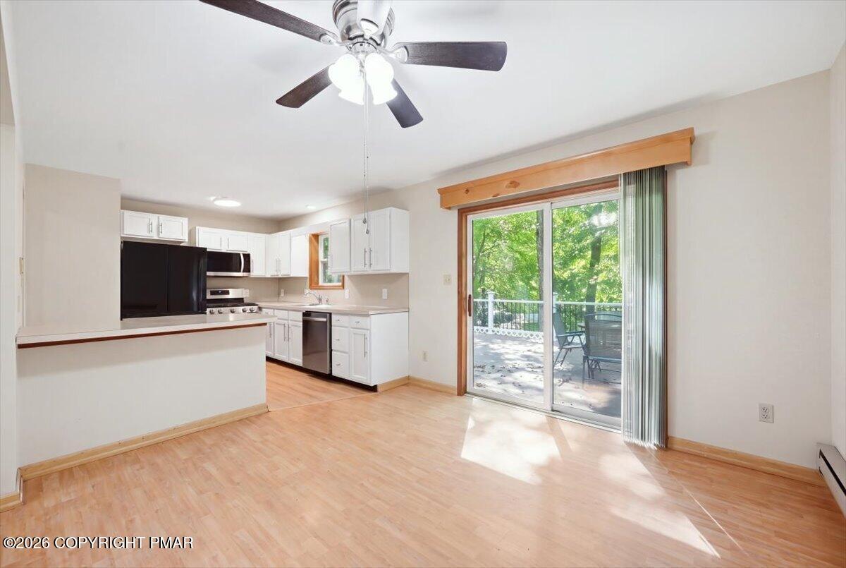 Open kitchen and dining area with white cabinets, wood floors, and a sliding door to a tree-lined deck.