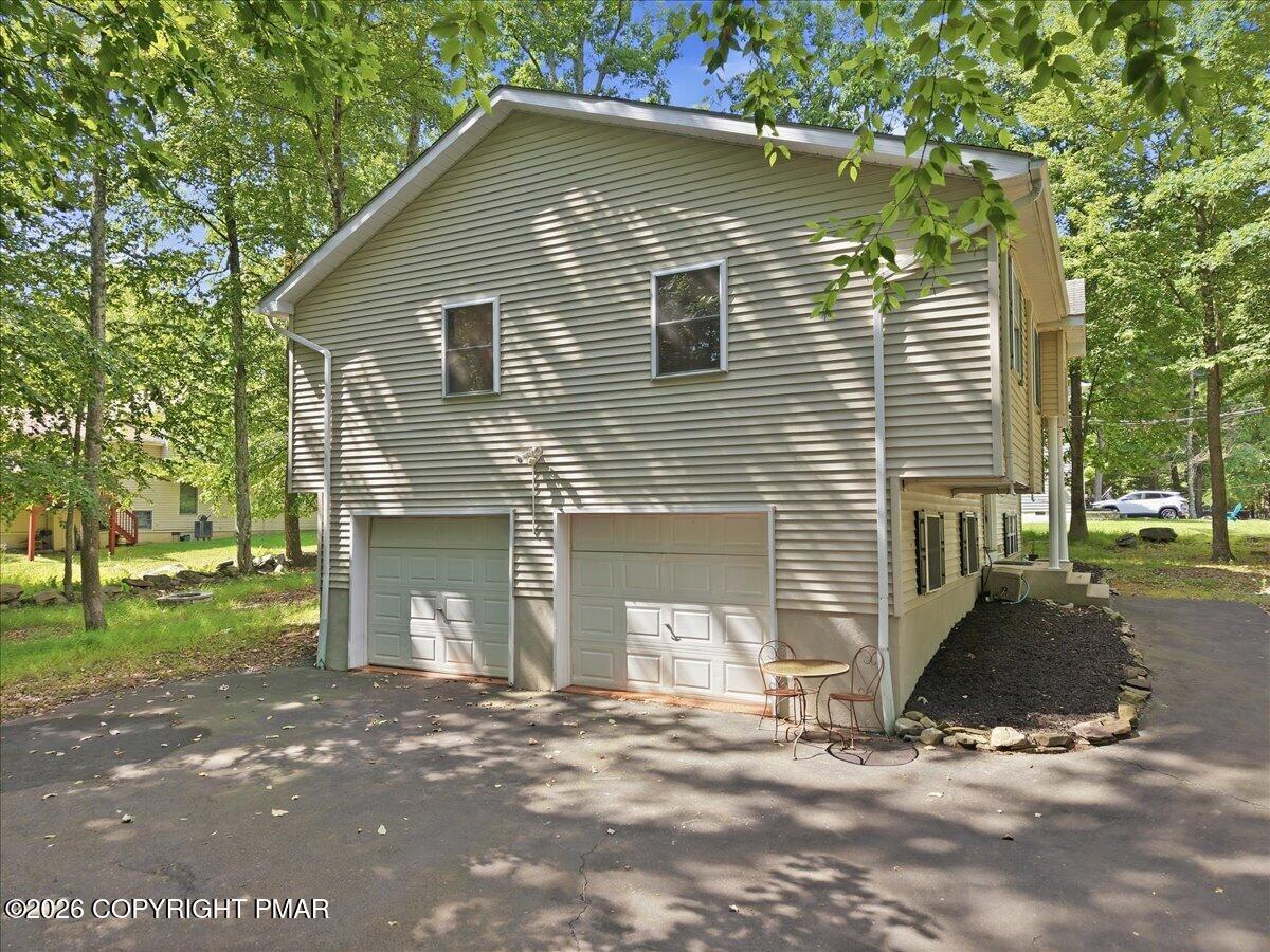 House exterior with two garage doors and a paved driveway shaded by mature trees.