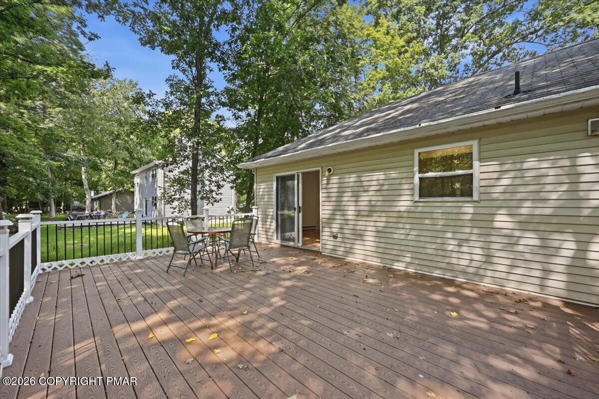 Wood deck with patio table and chairs beside a light-sided home, shaded by mature trees.