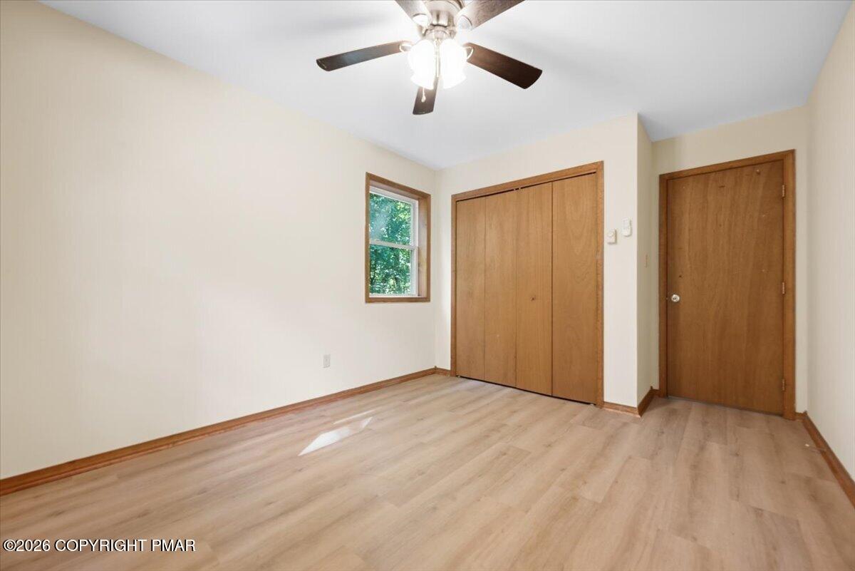 Empty bedroom with wood-look floors, a double-door closet, and a ceiling fan.