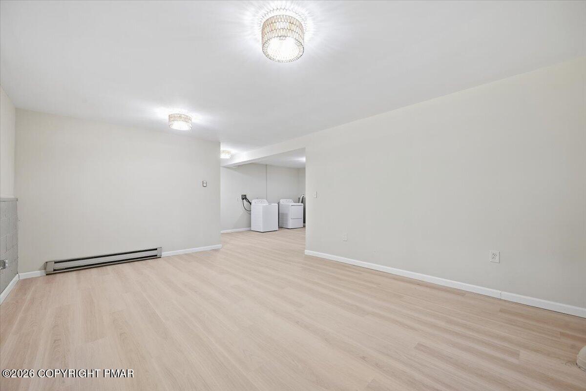 Empty finished room with pale wood-look flooring and a washer and dryer in the back.