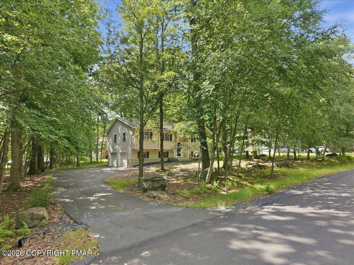 Two-story house among mature trees, with a curved driveway and wooded frontage.