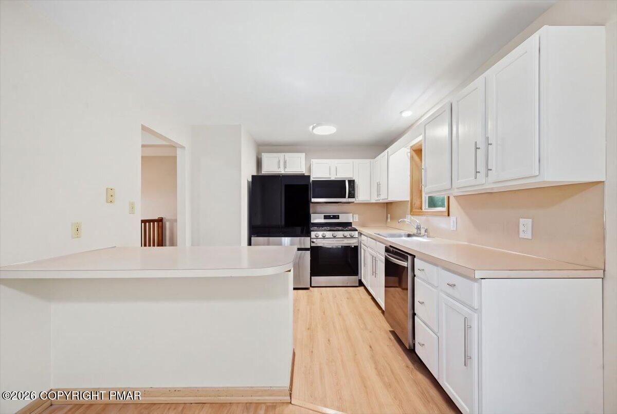 Kitchen with white cabinetry, a peninsula, stainless steel appliances, and light wood flooring.