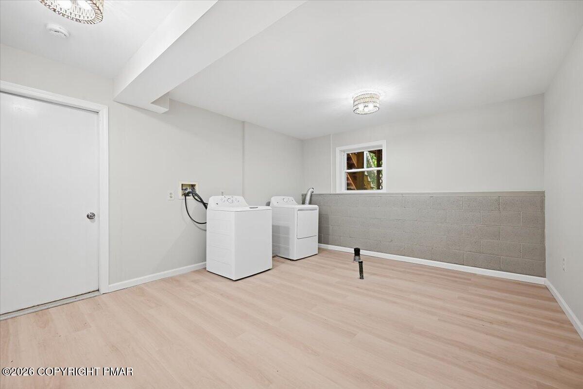 Laundry room with a white washer and dryer, pale flooring, and a low cinderblock wall.
