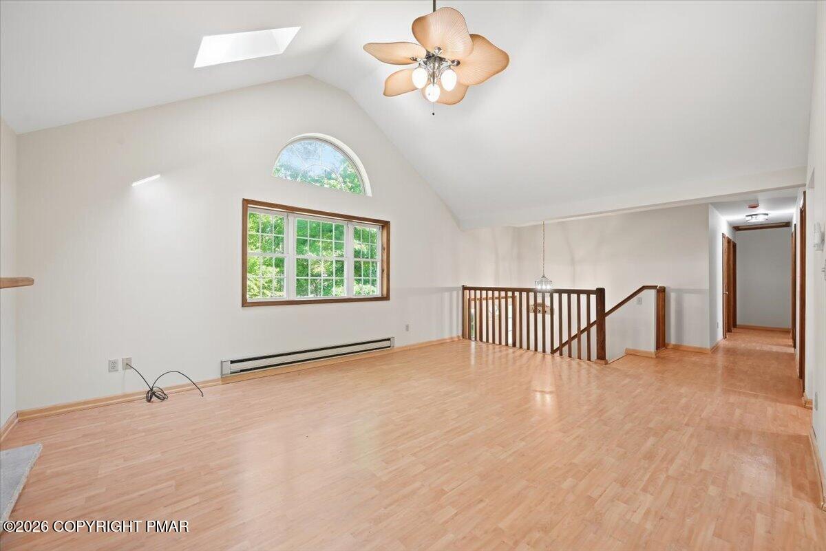 Vacant upstairs living area with vaulted ceiling, skylight, large window, and wooden stair railing.