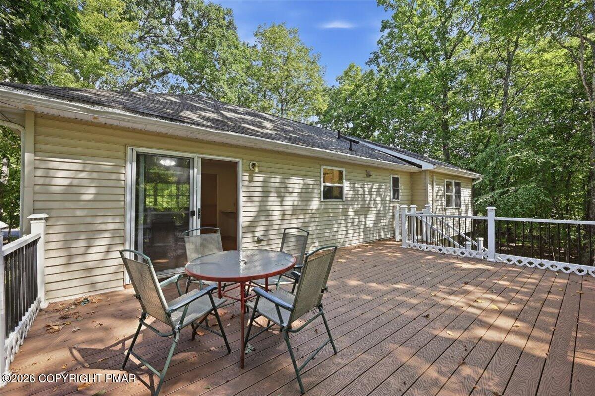 Spacious wood deck with outdoor dining set beside a beige-sided home, surrounded by trees.