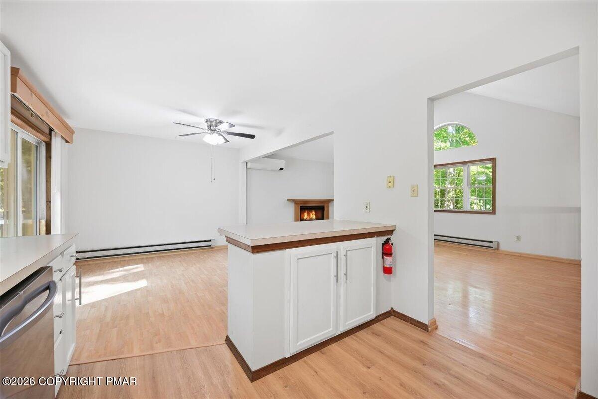 Vacant kitchen with a white peninsula opening to a living area with a fireplace.