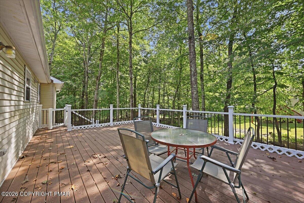 Furnished wooden deck with patio seating overlooking a leafy wooded backyard.