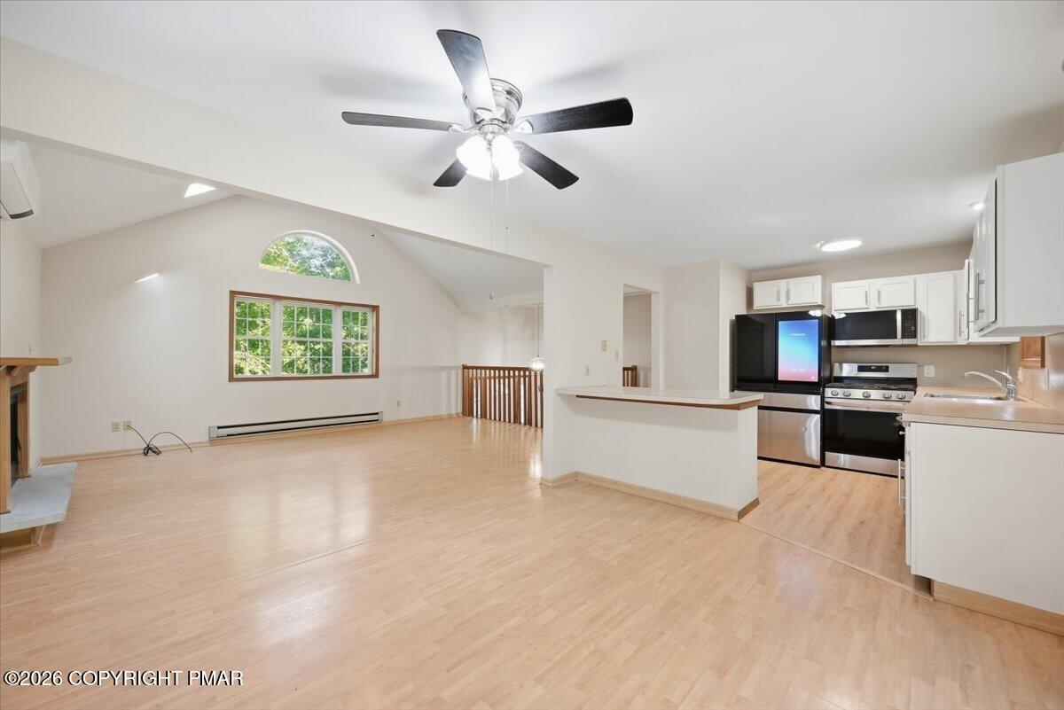Open-plan living area and kitchen with vaulted ceiling, light wood floors, and white cabinetry.