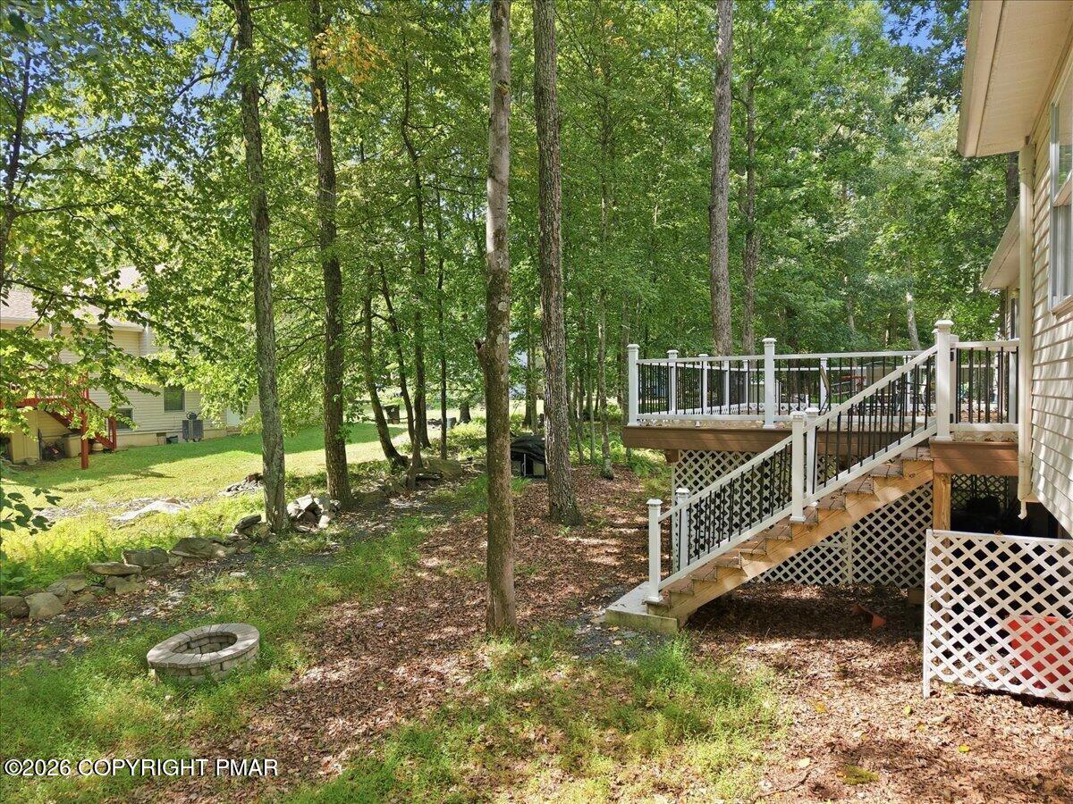 Wooded backyard with a raised deck, white railings, stairs, and a small stone fire pit.