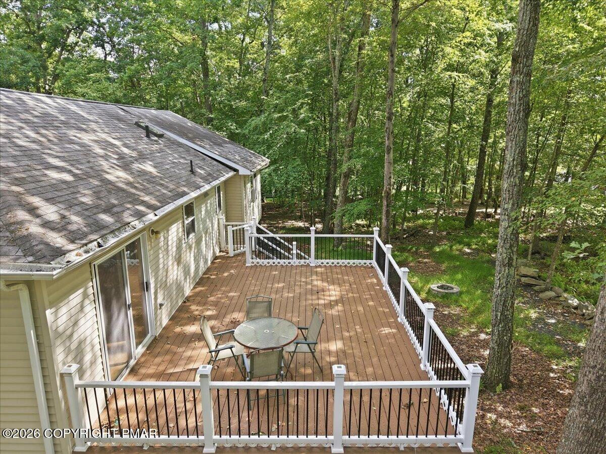 Wooden deck with white railings, patio table and chairs, and a wooded setting.