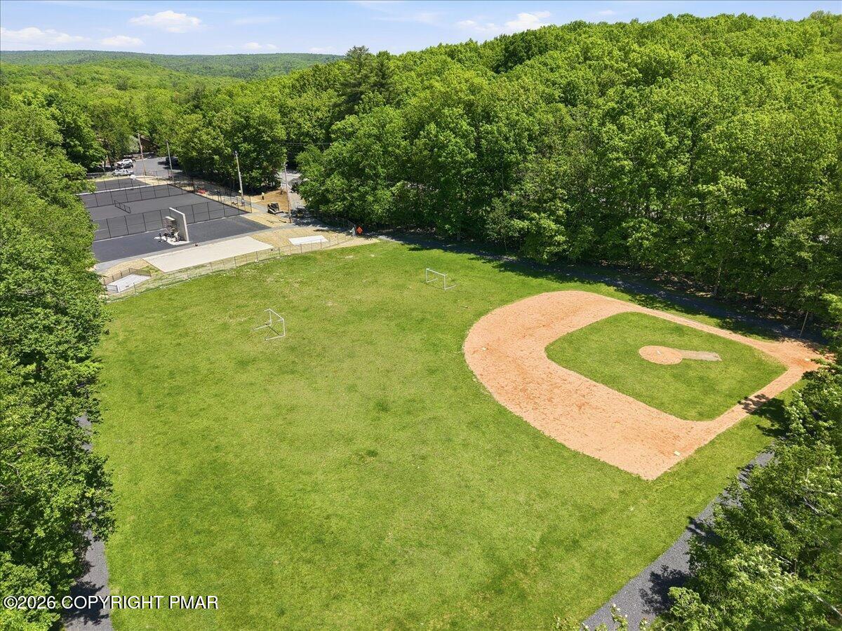 Aerial view of a wooded recreation area with a baseball diamond and fenced tennis courts.