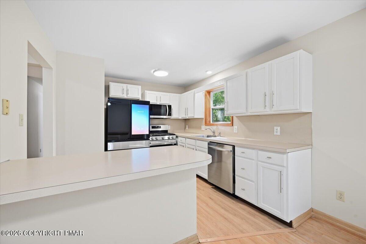 Kitchen with white cabinetry, a broad peninsula, stainless steel appliances, and light wood-look flooring.