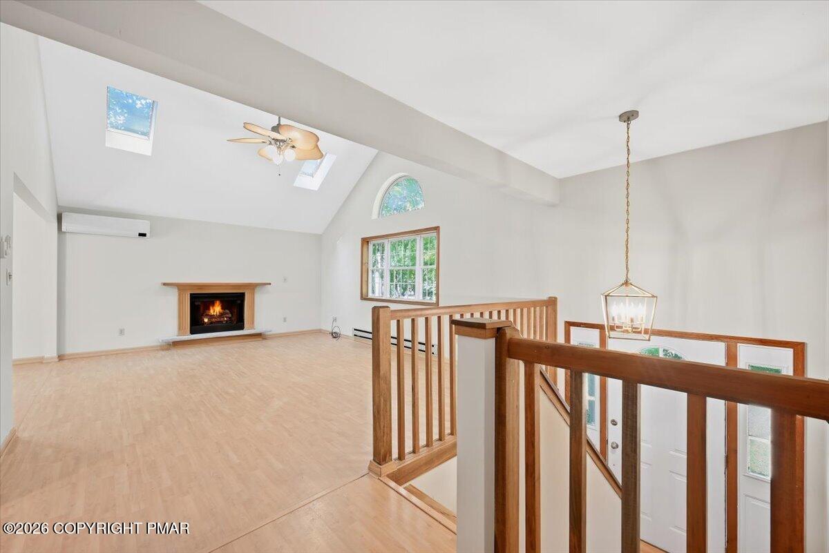 Unfurnished living room with a fireplace, vaulted ceiling, skylights, and wood stair railing.