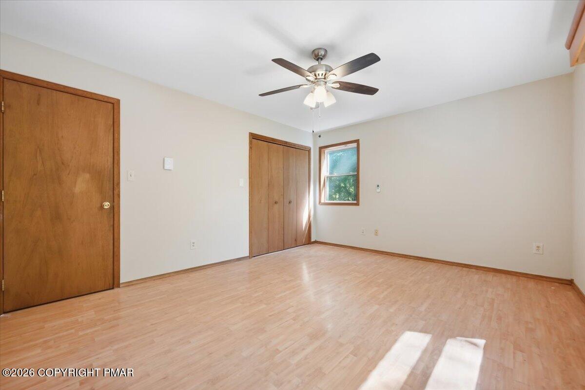 Empty bedroom with light wood floors, wood closet doors, and a ceiling fan.