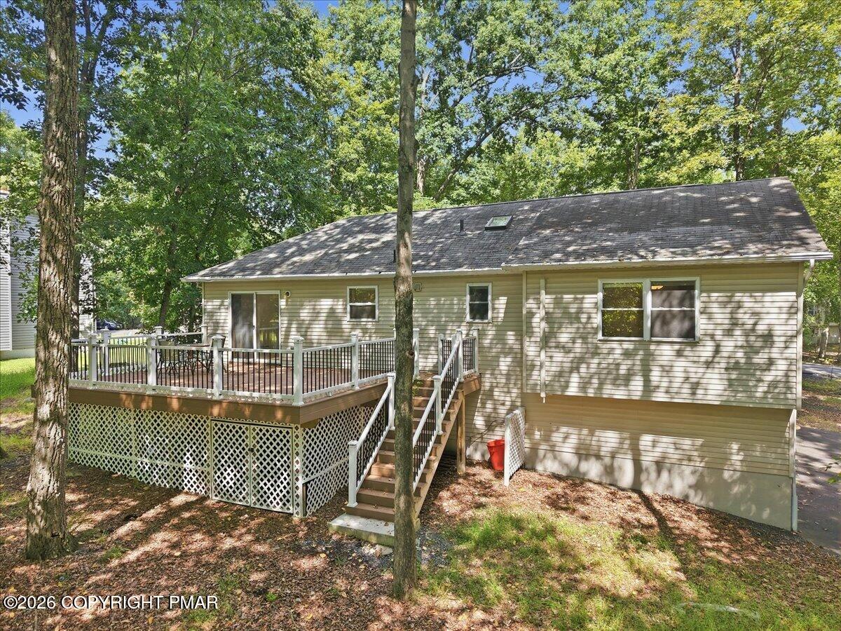 Rear of a light-colored home with a raised deck and lattice skirting beneath mature trees.