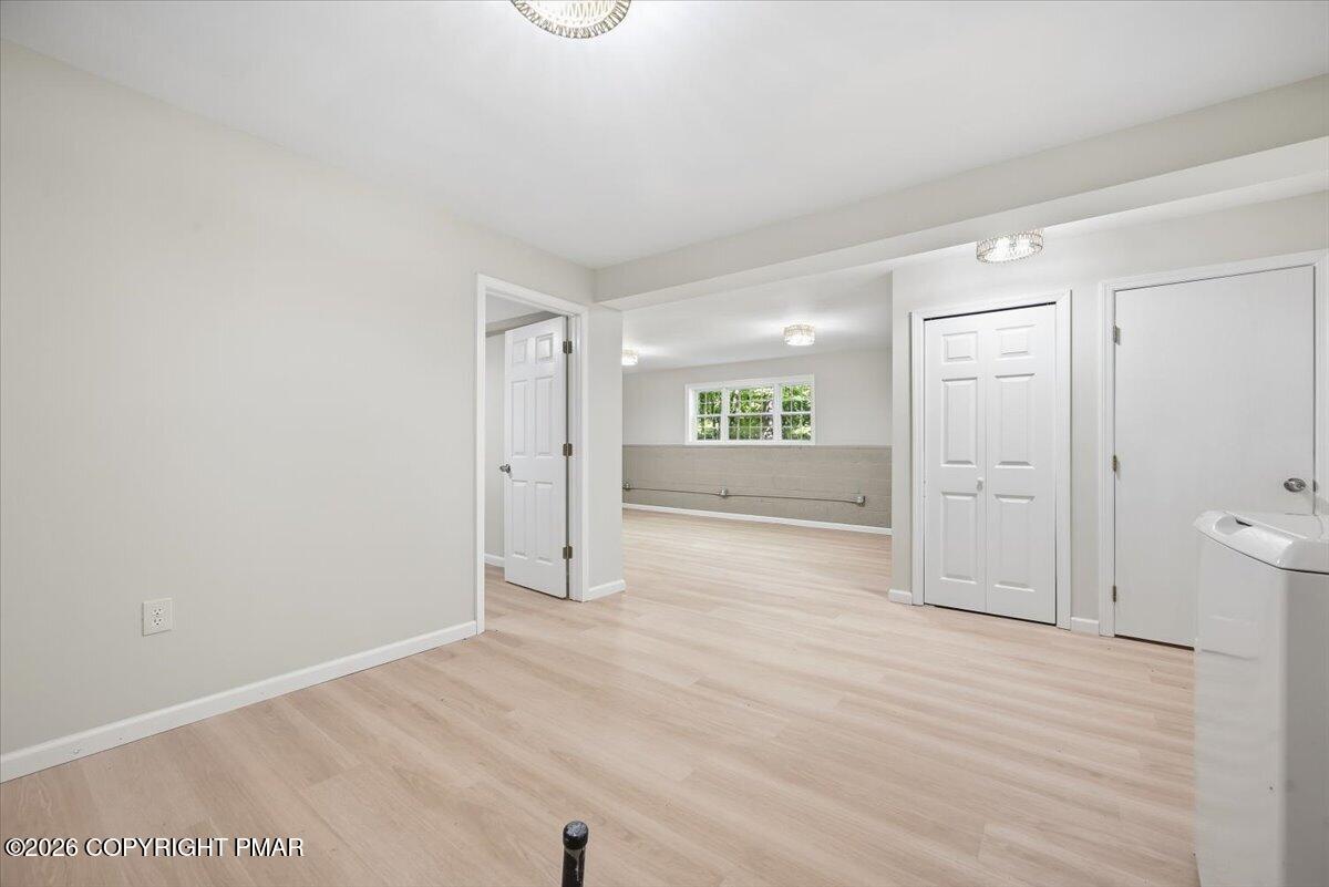 Laundry room with pale wood-look floors, a tiled wall and grab bar, and a white appliance.