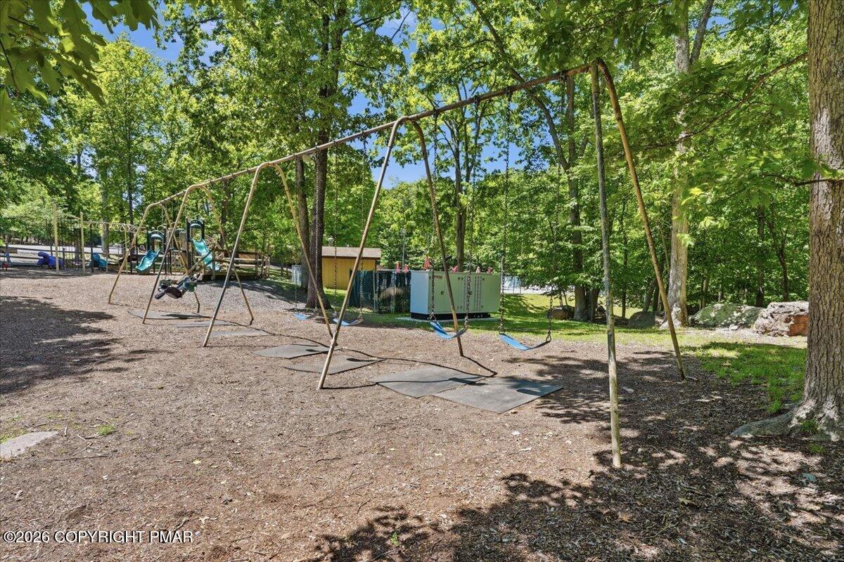 Wooded playground with a long swing set and slides beneath mature trees.