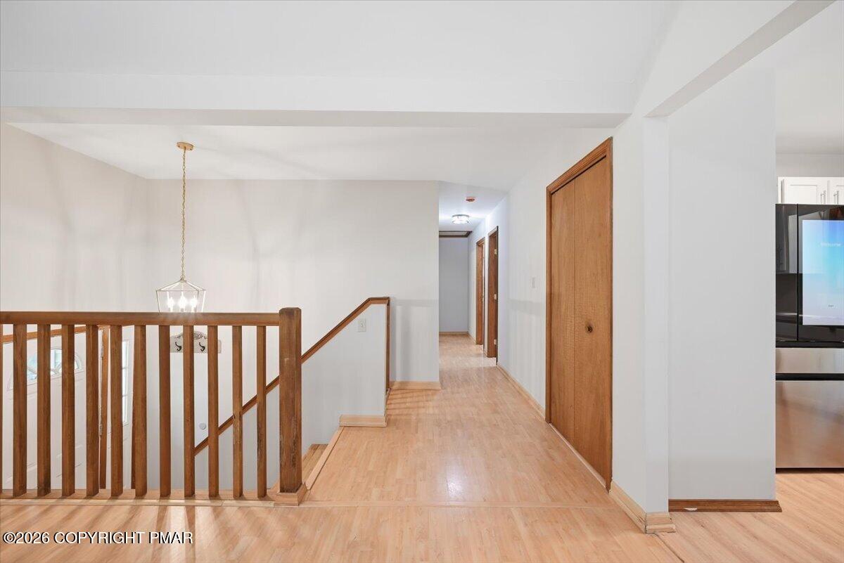 Landing and hallway with light wood floors, wooden stair railing, and a pendant light.