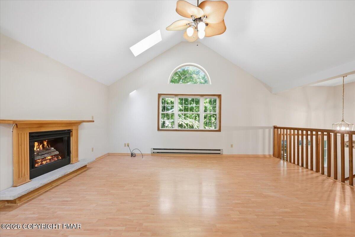 Empty living room with a vaulted ceiling, fireplace, light wood flooring, and large windows.