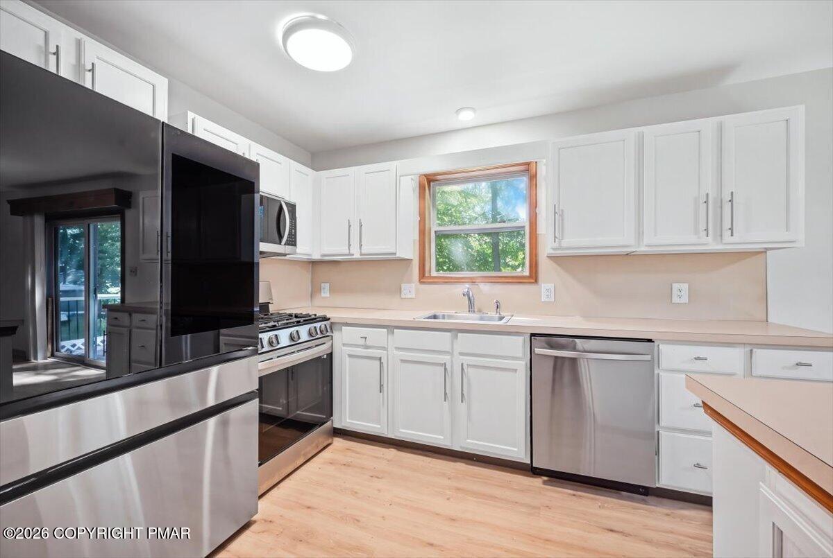 Kitchen with white cabinets, stainless steel appliances, and a window above the sink.