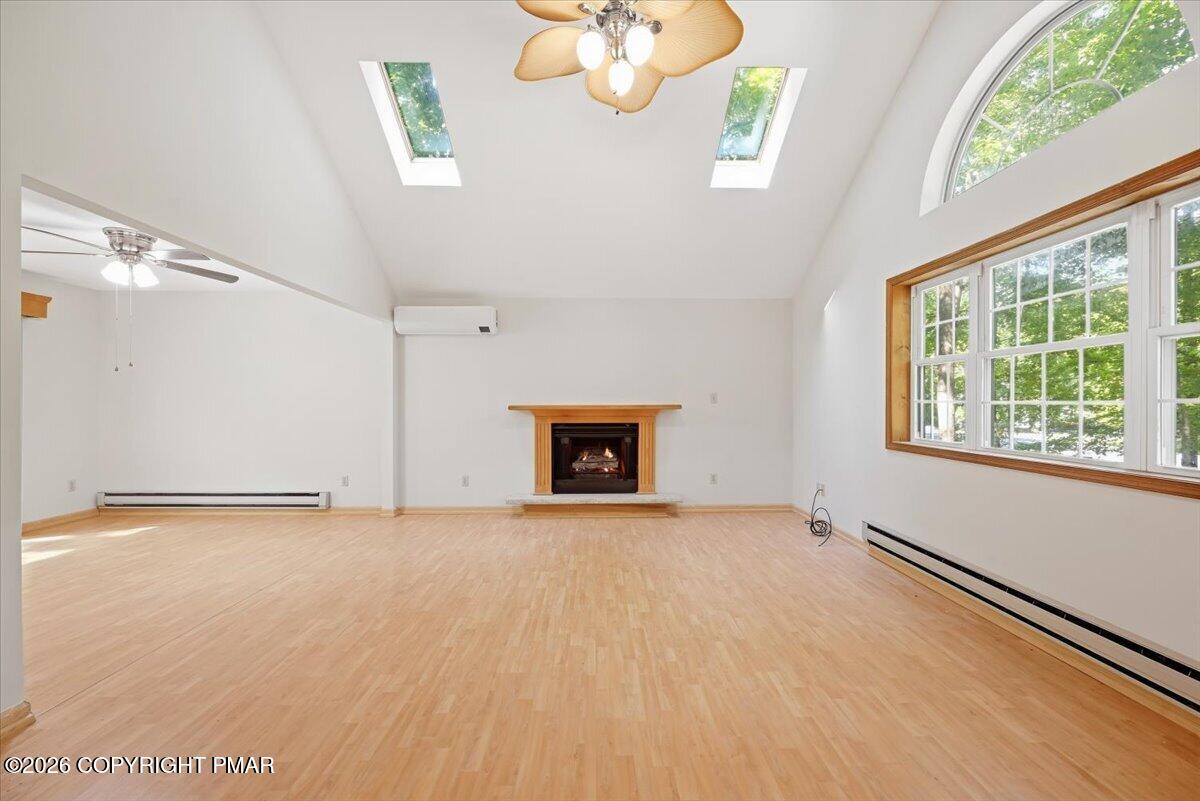 Vacant living room with a fireplace, vaulted skylit ceiling, and large arched window.