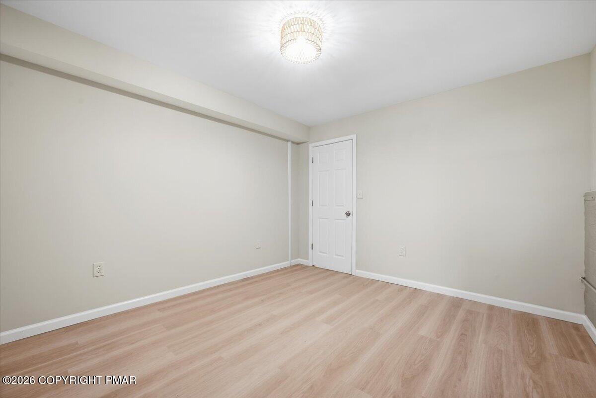 Empty room with pale wood-look flooring, neutral walls, and a white paneled door.