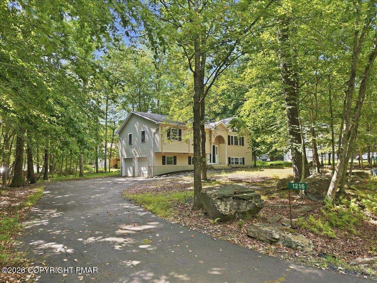 Split-level home among mature trees, with a paved driveway and green 1216 address sign.