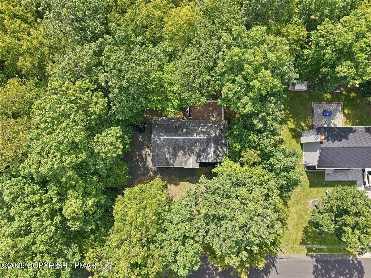 Aerial view of a wooded residential lot with a house and backyard deck.
