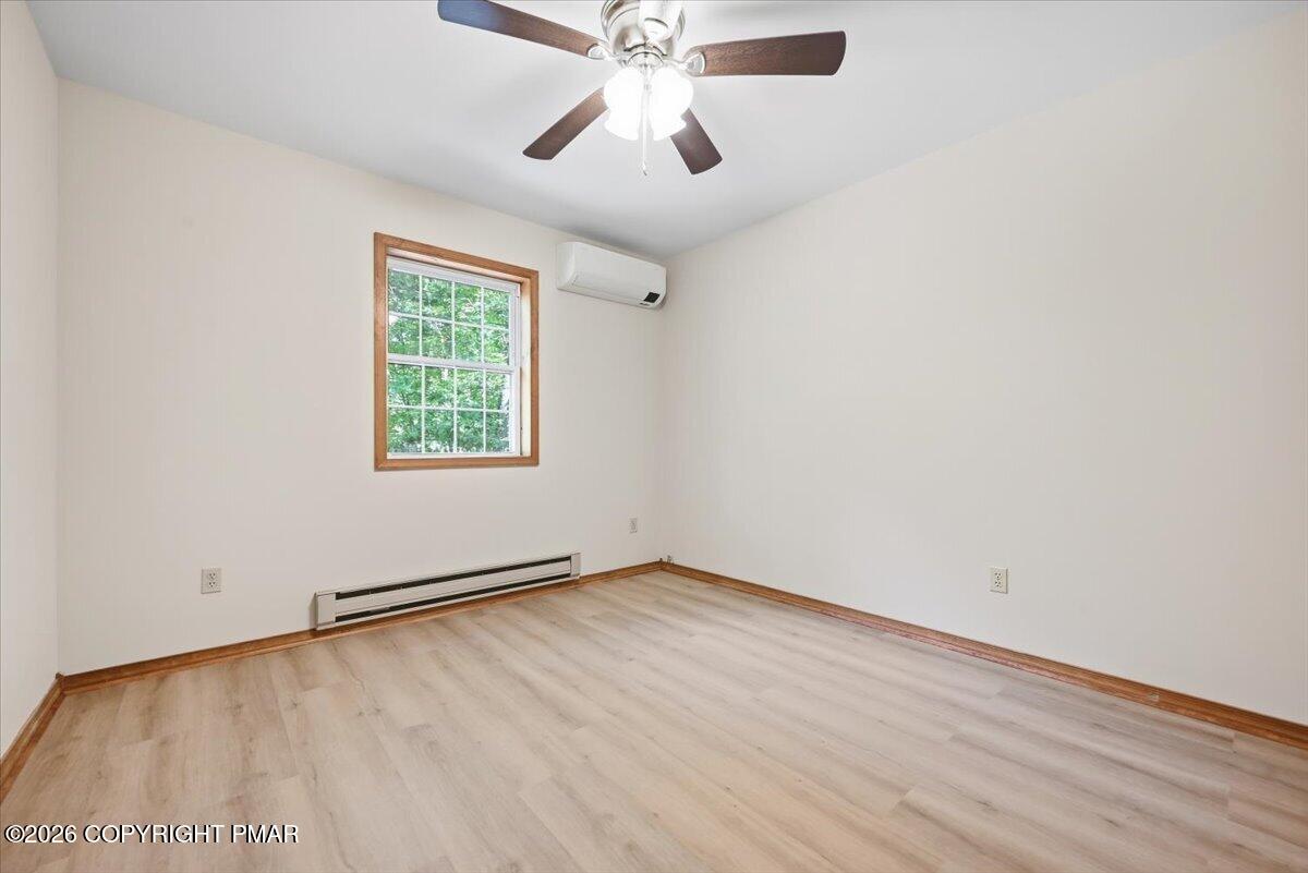 Vacant bedroom with light wood-look flooring, a wood-trimmed window, ceiling fan, and wall-mounted mini-split.
