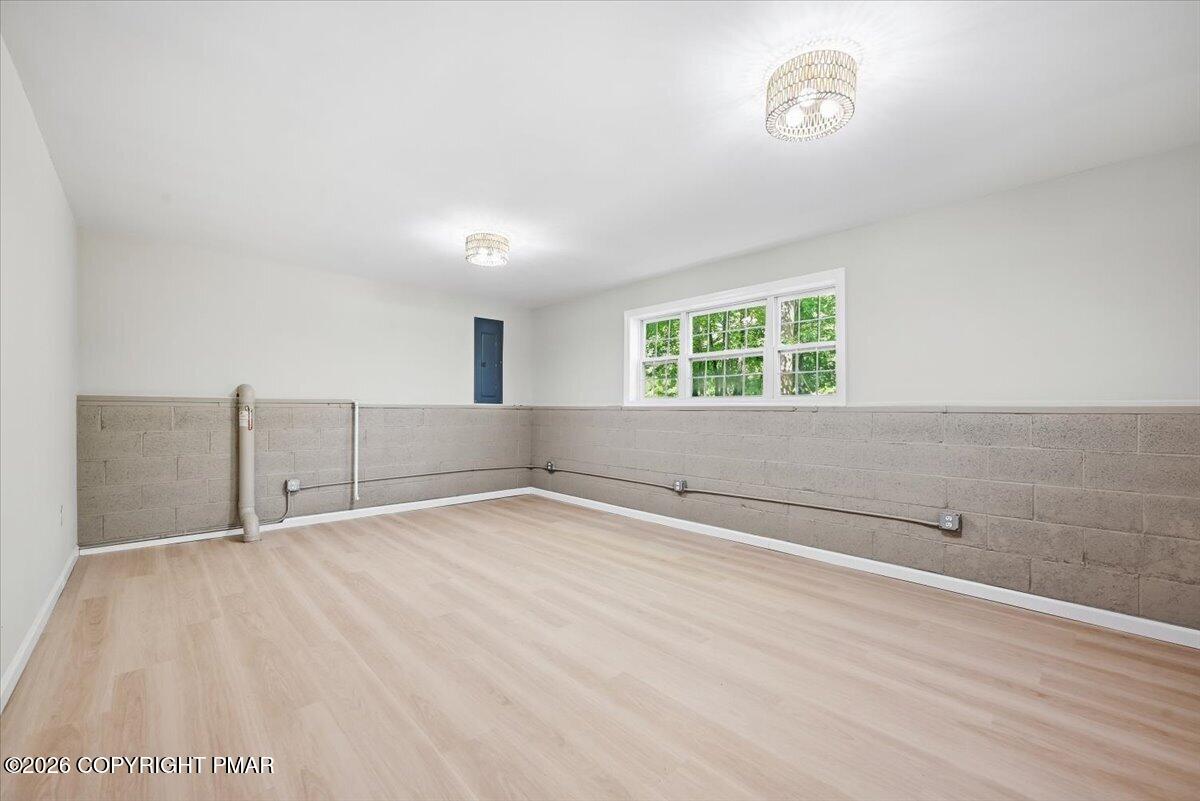 Vacant room with pale wood-look flooring, concrete block lower walls, and a window overlooking trees.
