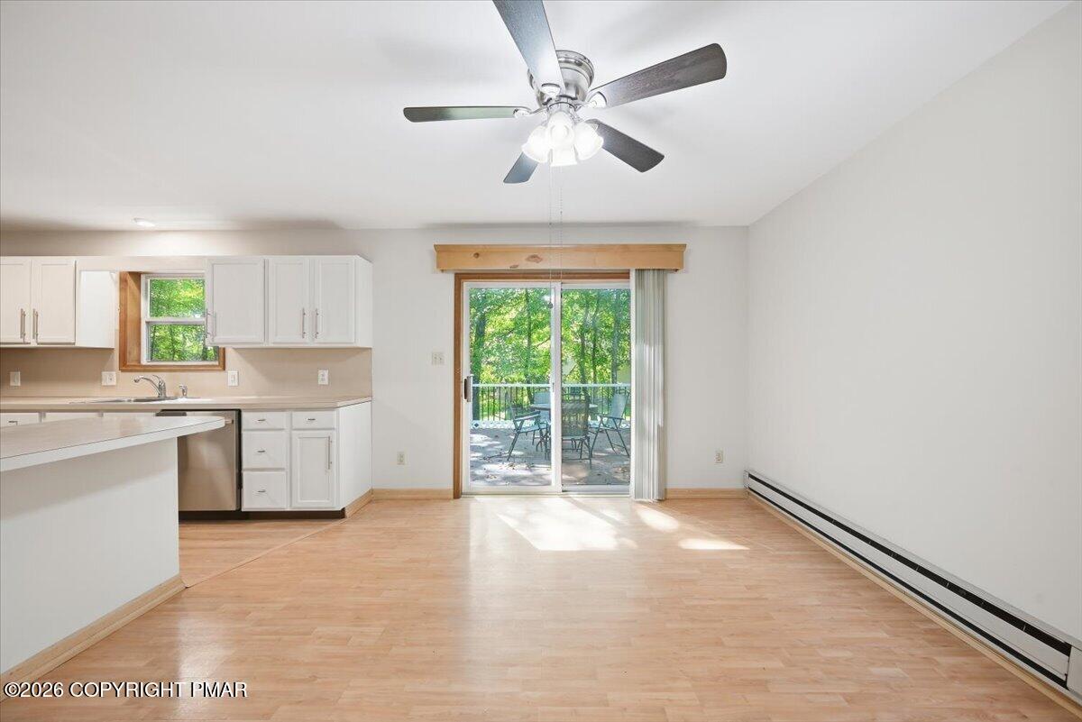Kitchen and dining area with white cabinets, light wood floors, and sliding doors to a wooded deck.