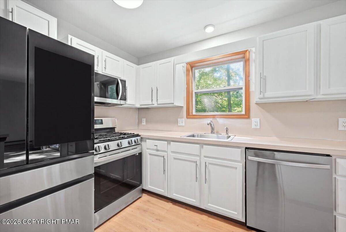 Kitchen with white cabinets, stainless steel appliances, and a wood-trimmed window over the sink.