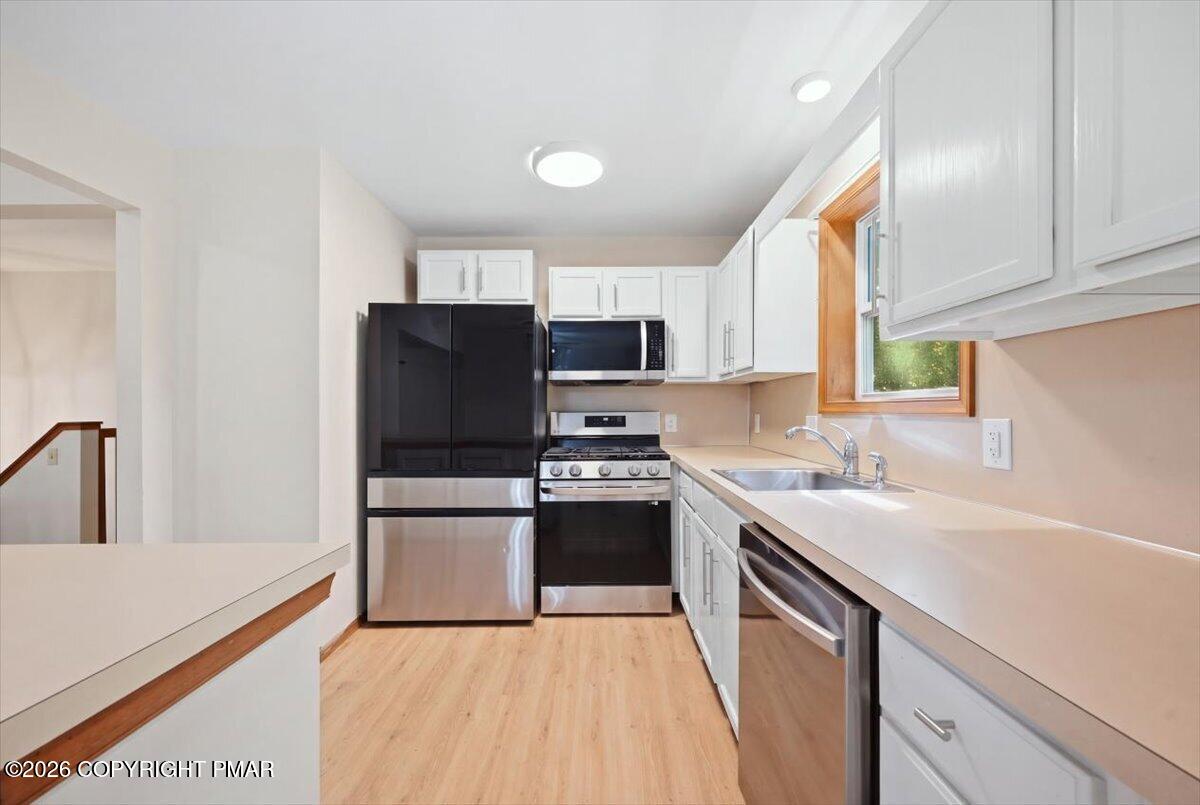 Kitchen with white cabinets, stainless steel appliances, and a sink beneath a wood-trimmed window.