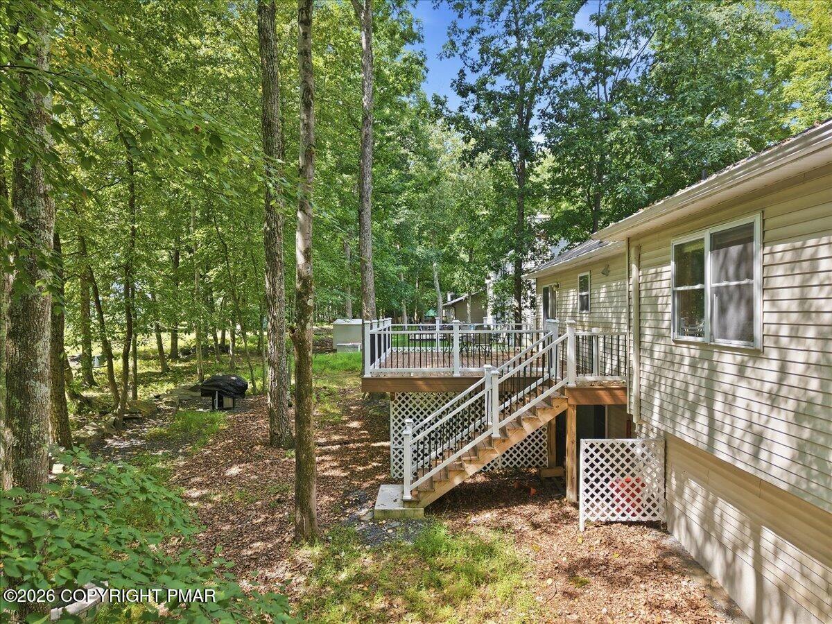 House rear with raised deck and stairs amid a leafy wooded yard.