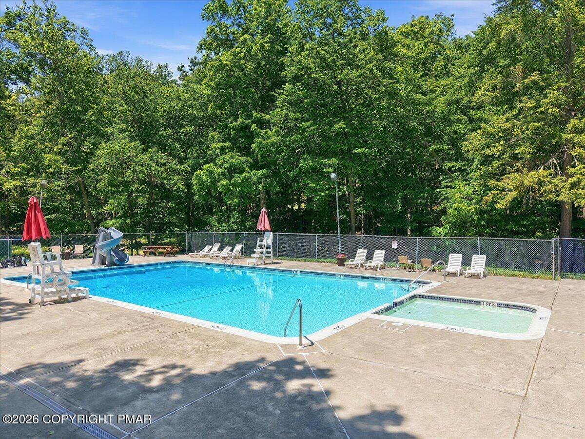 Outdoor pool with a slide and shallow wading area beside a wooded backdrop.