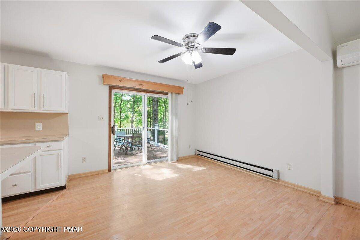 Vacant living area with light wood floors and sliding glass doors opening to a wooded deck.