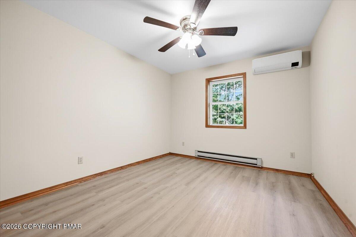 Empty bedroom with light wood-look flooring, a ceiling fan, and a wall-mounted mini-split unit.