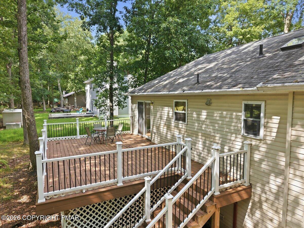Rear exterior with a raised wood deck, white railings, patio table, and wooded yard.