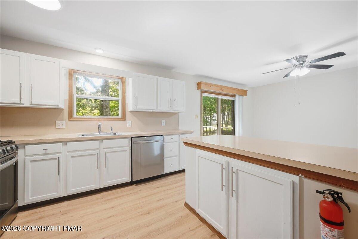 Kitchen with white cabinets, a large island, stainless steel dishwasher, and sliding glass doors to trees.