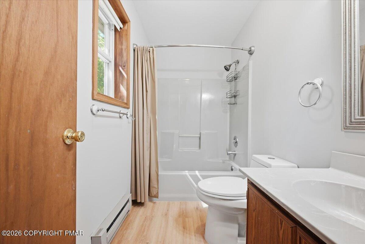 Bathroom with a tub and shower, toilet, and wood-front vanity beside a window.