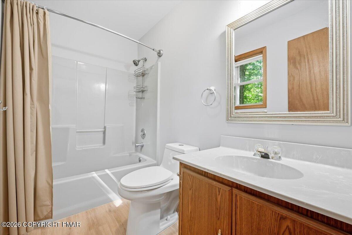 Bathroom with a white tub and shower, beige curtain, and wood vanity beneath a large framed mirror.