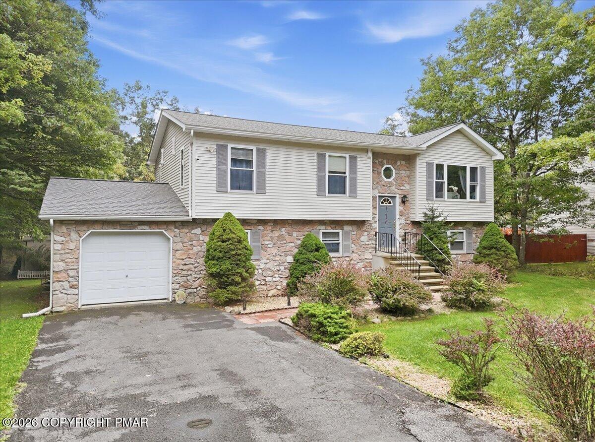 Split-level home with a stone lower facade, attached garage, and landscaped front yard.