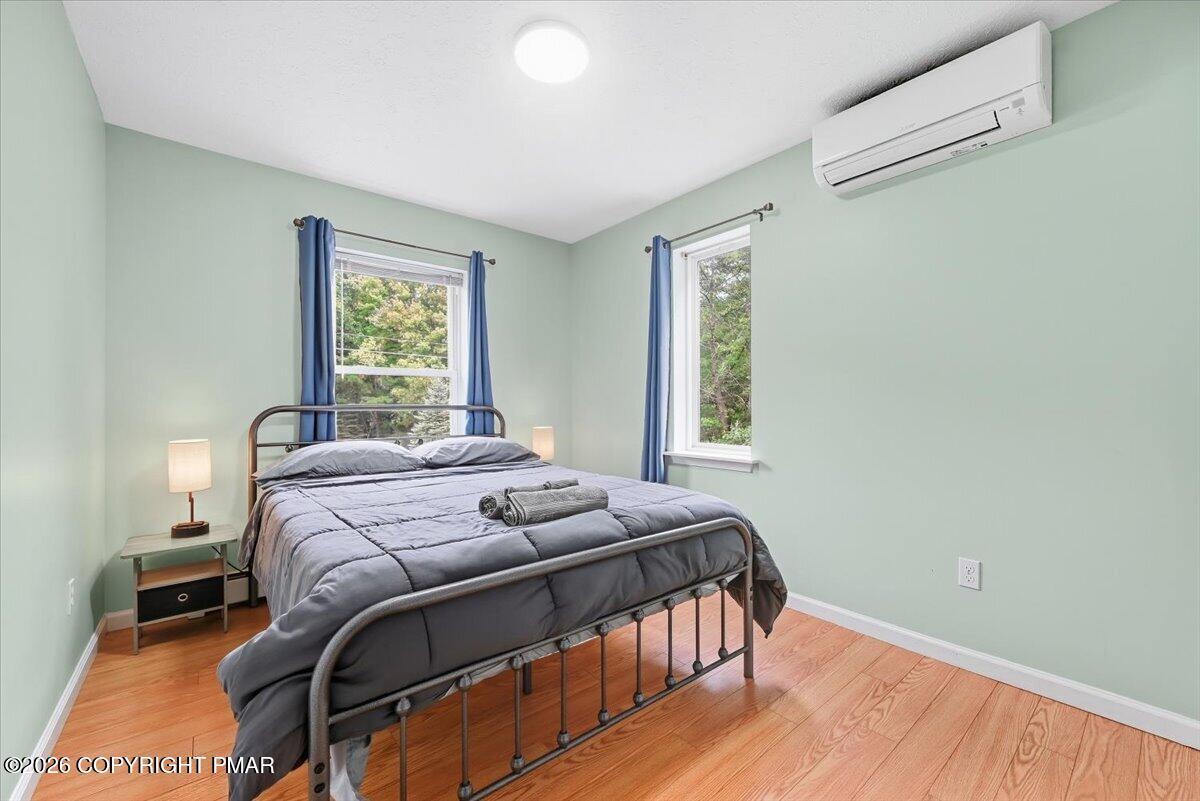 Bedroom with gray bedding, blue curtains, two windows, and a wall-mounted air conditioner.