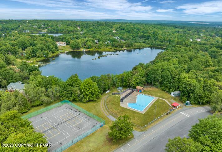 Aerial view of a wooded lake, community pool, and tennis courts.
