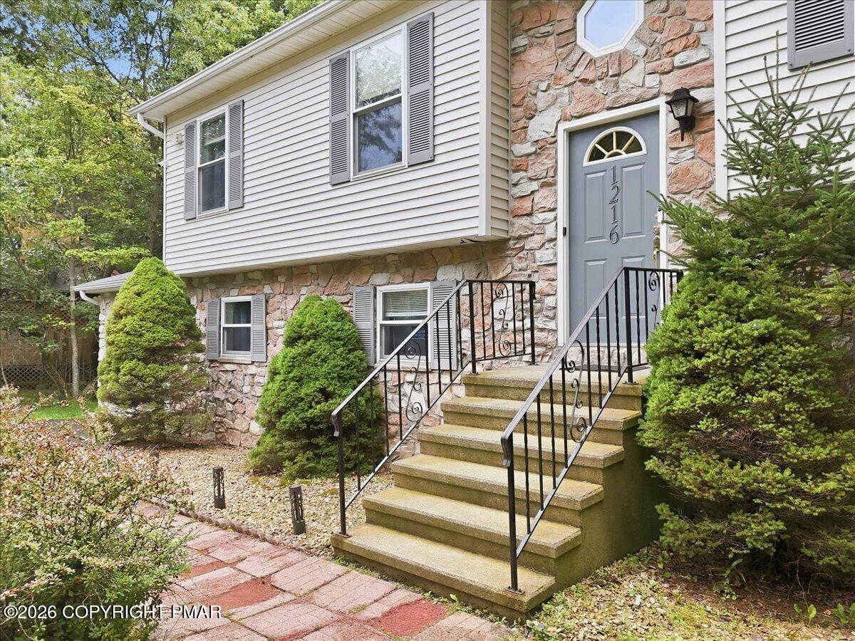 Stone-and-siding home with front steps, black railings, and a brick walkway.