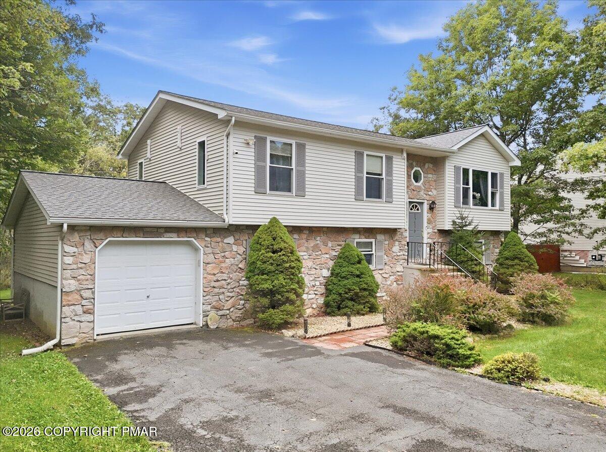 Split-level home with stone facade, attached garage, and landscaped front yard.